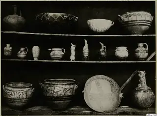 Three shelves of ancient pottery vessels and small figures from Cyprus, shown in the Cyprus Museum, with painted bands, zigzags and spirals.
