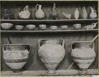 Shelves of painted pottery: animal-shaped and spouted vessels, seven small bowls, and three large two-handled jars
