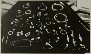 Corroded metal rings, pins and arrowheads laid out in rows on a black cloth