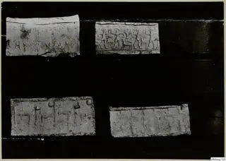 Four pale rectangular pieces with impressed designs of figures and signs, laid on a dark background.