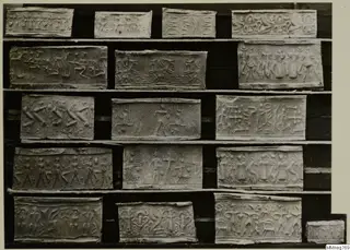 Rows of pale rectangular seal impressions with carved figures and animals, arranged on a dark board.