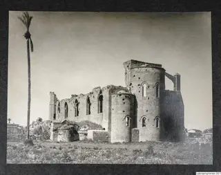 Ruined stone church seen from the side, with a tall palm tree beside it and grass in the foreground