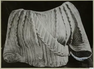 Carved marble sculpture fragment with deep drapery folds and a broken edge at the right end