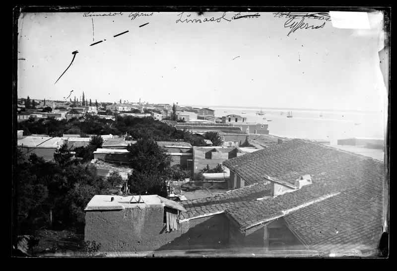View over tiled and flat roofs of Limassol towards the sea, with small ships moored in the bay