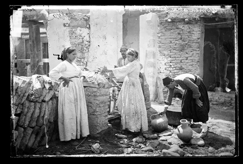 Women and a man beside a well with mud-brick walls and clay jugs on the ground