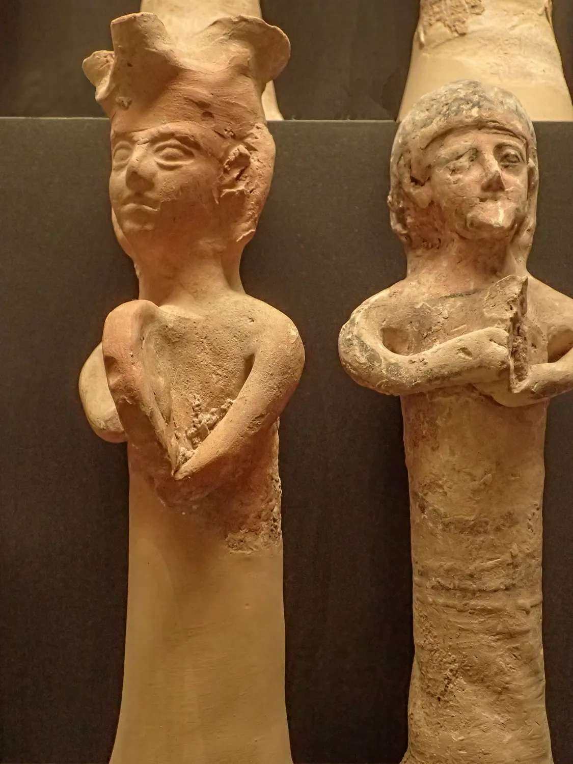 Two Cypriot terracotta votary figures with cylindrical bodies and arms folded over offerings, one in a tall flaring crown, from the sanctuary of Astarte at Kamelarga; Cypro-Archaic, Ashmolean Museum, Oxford.