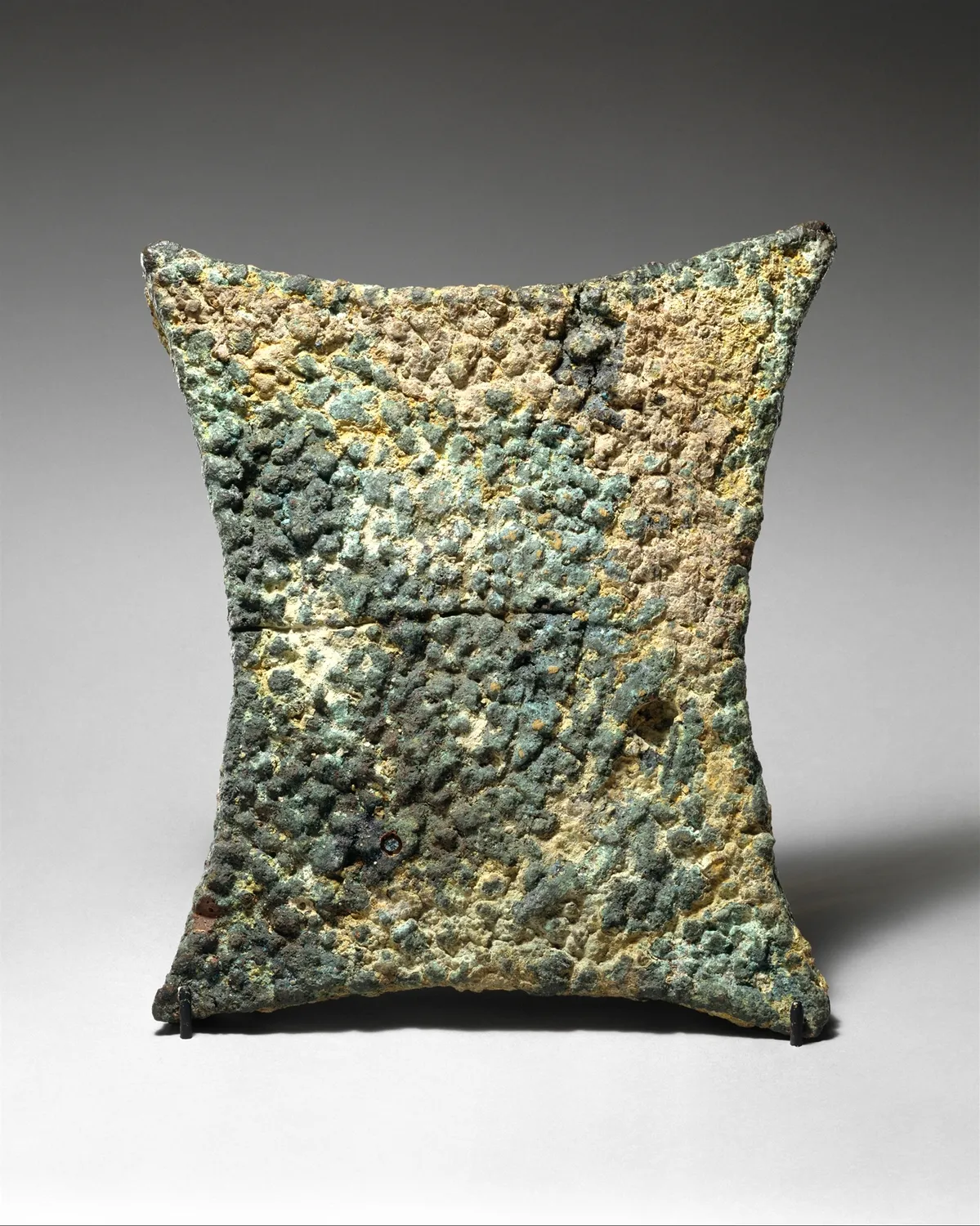 A copper oxhide ingot, a slab drawn out into a grip at each of its four corners, the surface rough and green with corrosion. Cypriot, Late Bronze Age (Metropolitan Museum of Art).