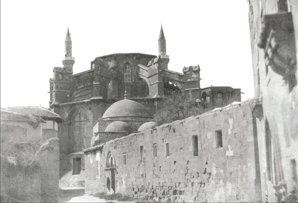 Louis de Clercq's 1859 photograph of the Cathedral of Saint Sophia at Nicosia, by then the Selimiye Mosque: the Gothic church seen from its apse end, two Ottoman minarets rising behind it, with the domed Bedesten and a low stone wall in the foreground.
