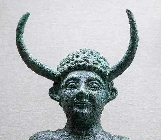 Green-patinated bronze statuette of a bearded warrior in a horned helmet, right arm raised holding a spear and left arm holding a small round shield, standing on a base cast in the shape of a four-eared oxhide copper ingot.