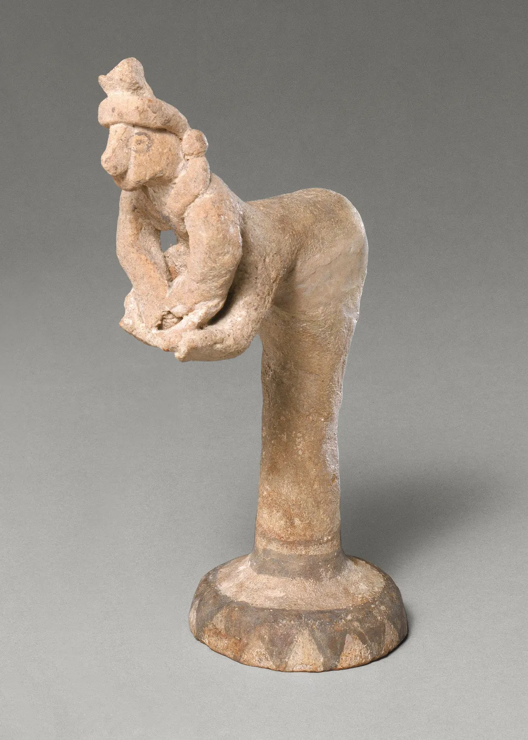 Cypriot terracotta figurine of a woman bent over a basin, working dough with both hands. A genre figure of the same kind as the seated potter.