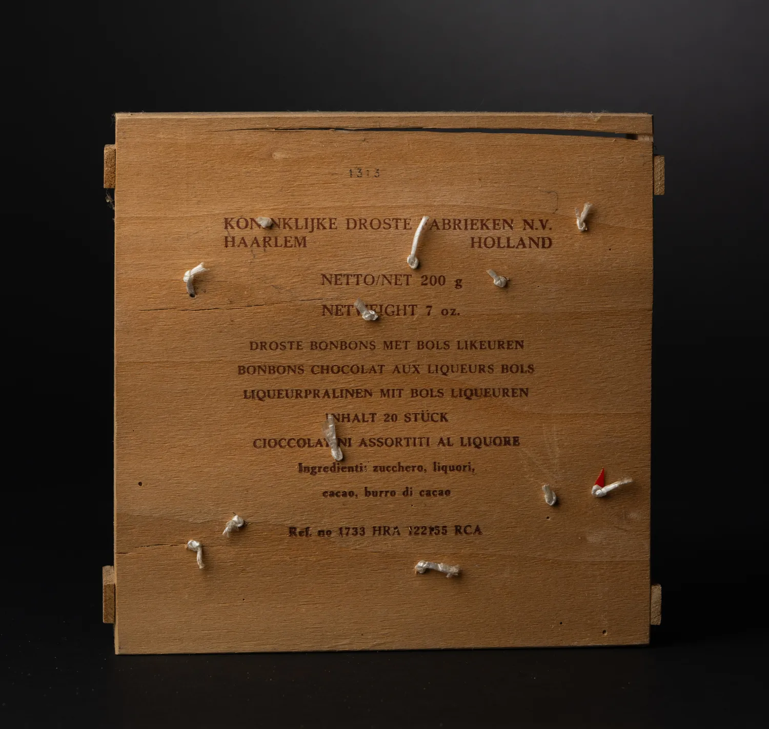 The reverse of the wooden Droste box, showing the plain grain of the pale wood and the finger-jointed corners, against a dark background.