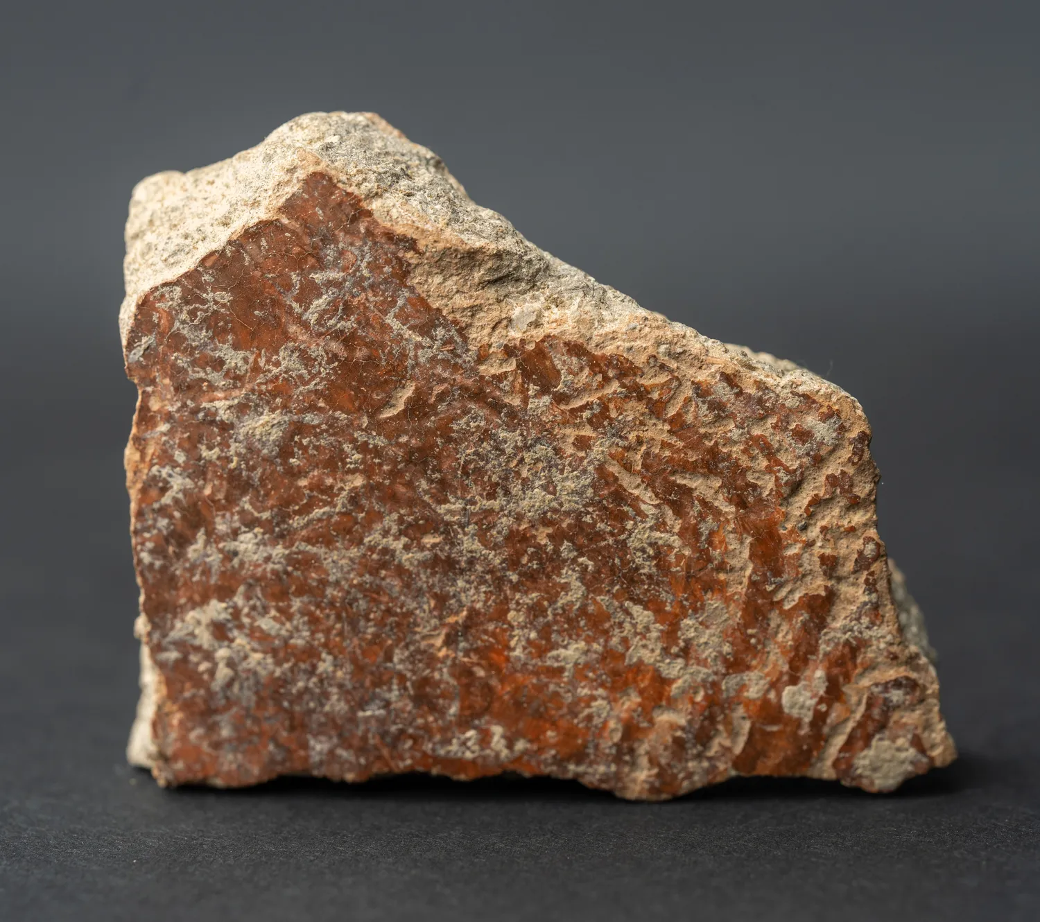 The convex outer face of a thick reddish potsherd, heavily encrusted with grey-white lime, the red slip and faint combed lines showing through the deposits.