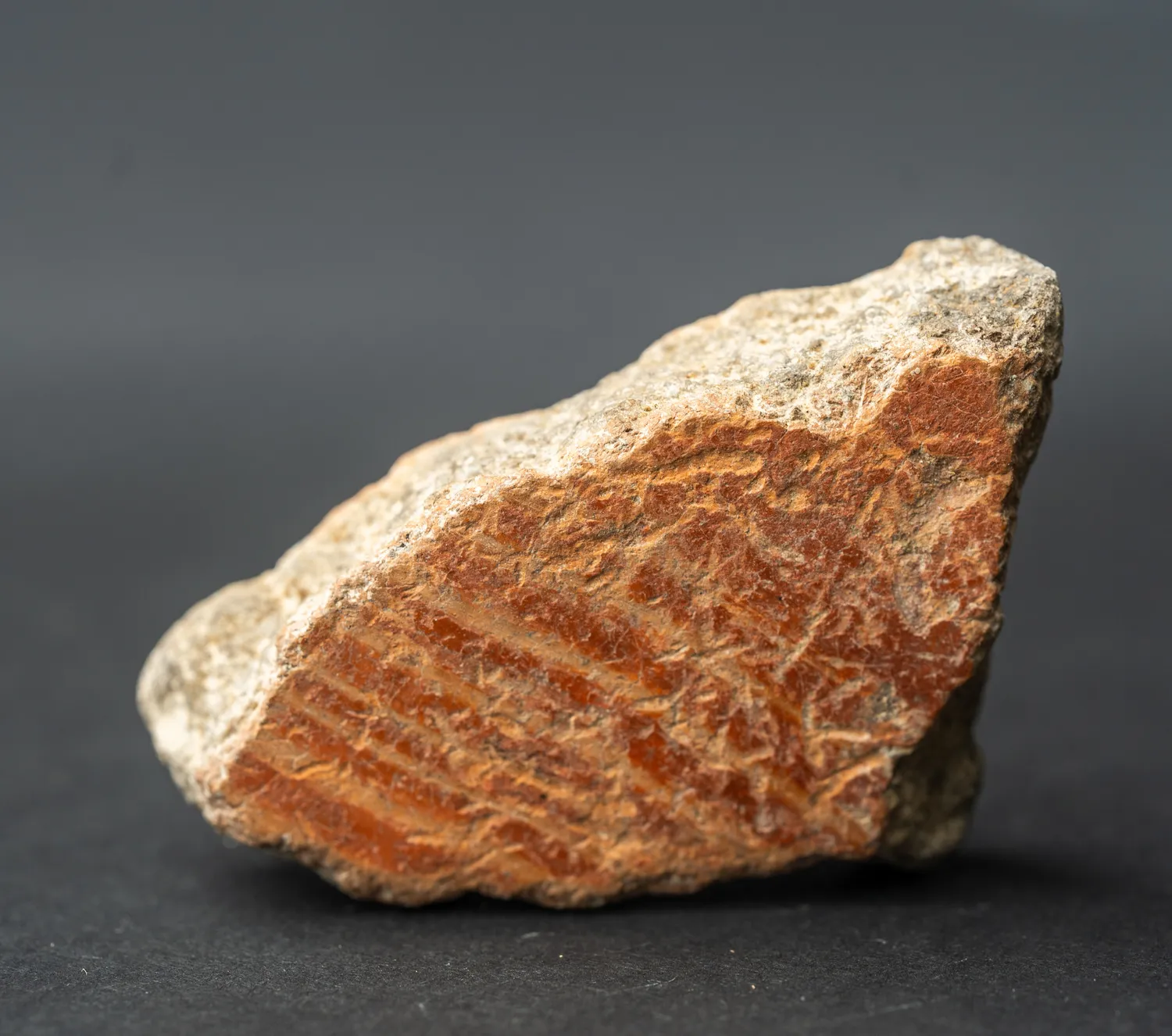 The exterior of a potsherd, its red-slipped surface mottled and lime-flecked, the combed bands faint beneath the encrustation.