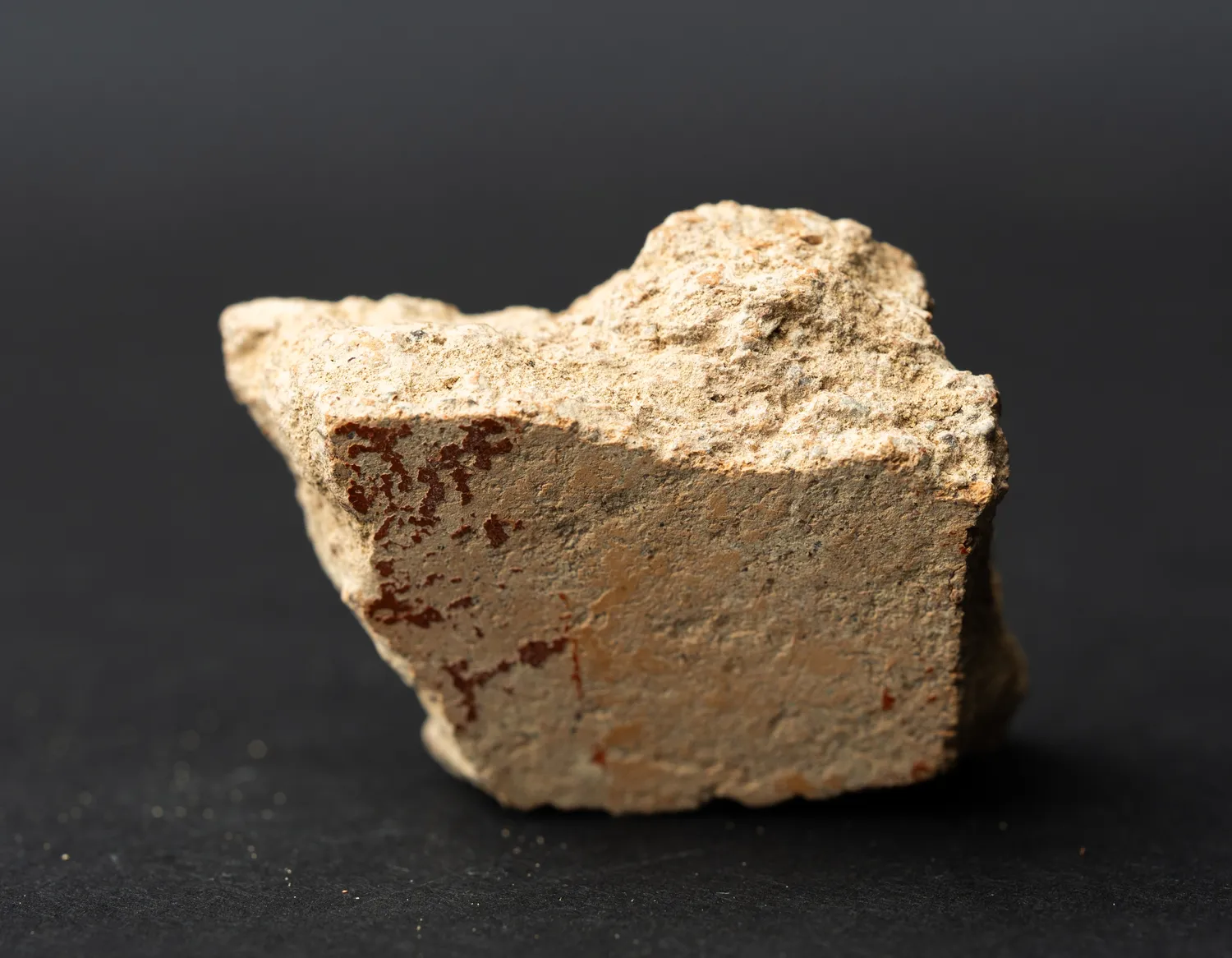 A potsherd with a curved profile, its interior showing combed banding under lime encrustation, the fabric a warm reddish-brown.