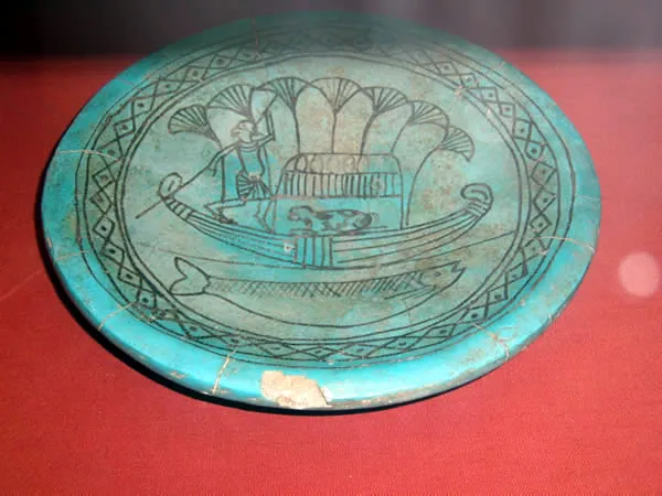 Faience dish from Enkomi Tomb 66, painted in black on a blue glaze with a man punting a papyrus boat, a bovine under a canopy and a fish below. British Museum. Photo: Udimu, CC BY-SA 3.0.