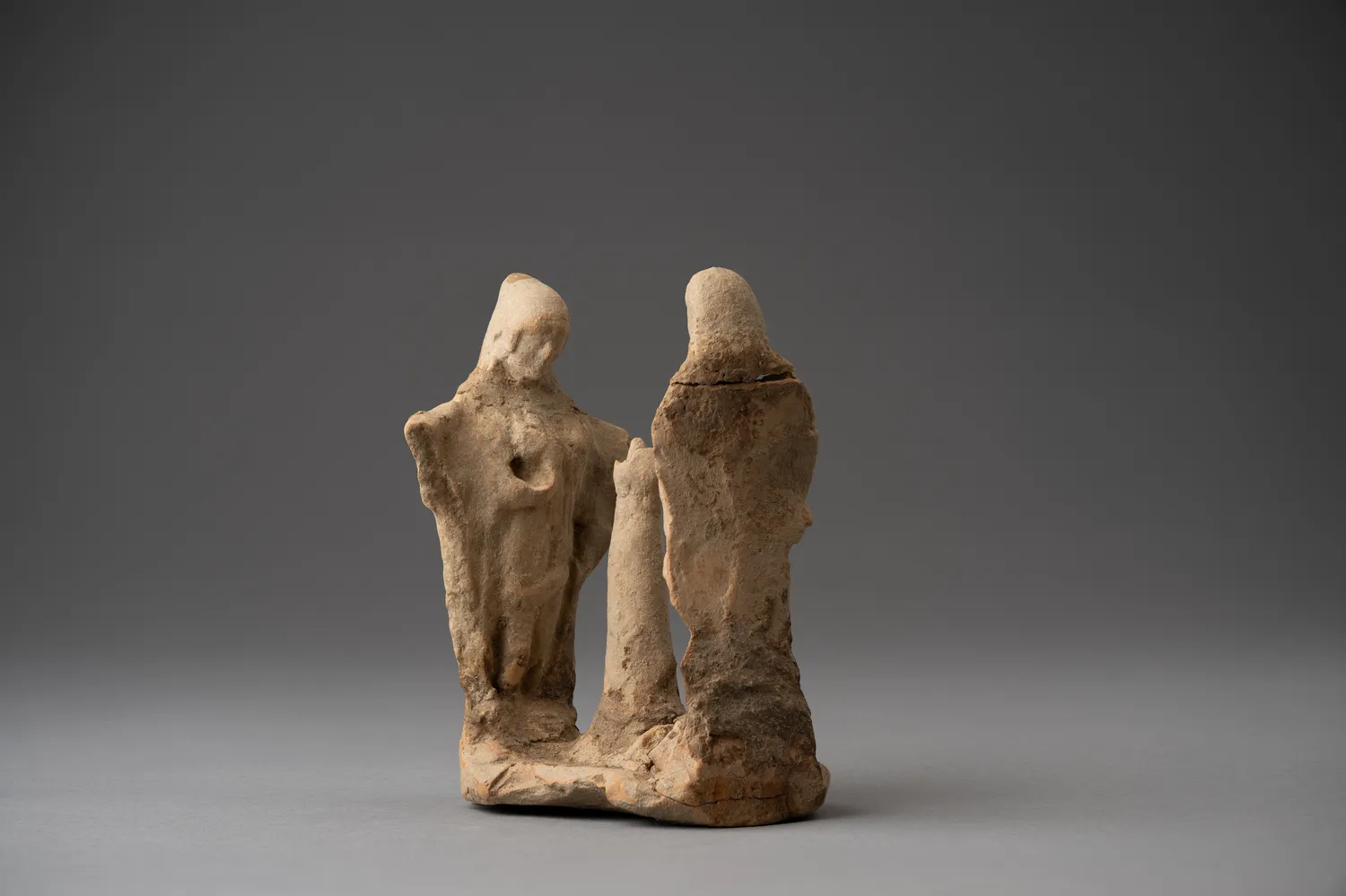 The Drakopoulos group seen from the front: two robed, hooded figures on a shared base, a breast modelled in low relief on the left figure, the broken central shaft standing between them.