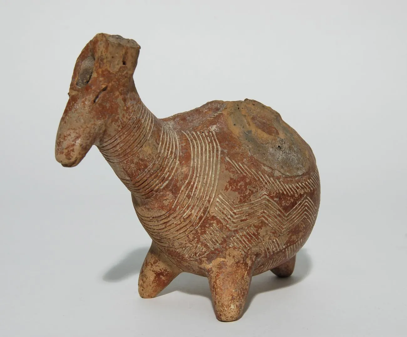 A Red Polished animal askos with a long-muzzled head, drilled eyes, and white-filled concentric circles and chevrons covering the body, standing on four short legs. British Museum, 1930,0422.2.