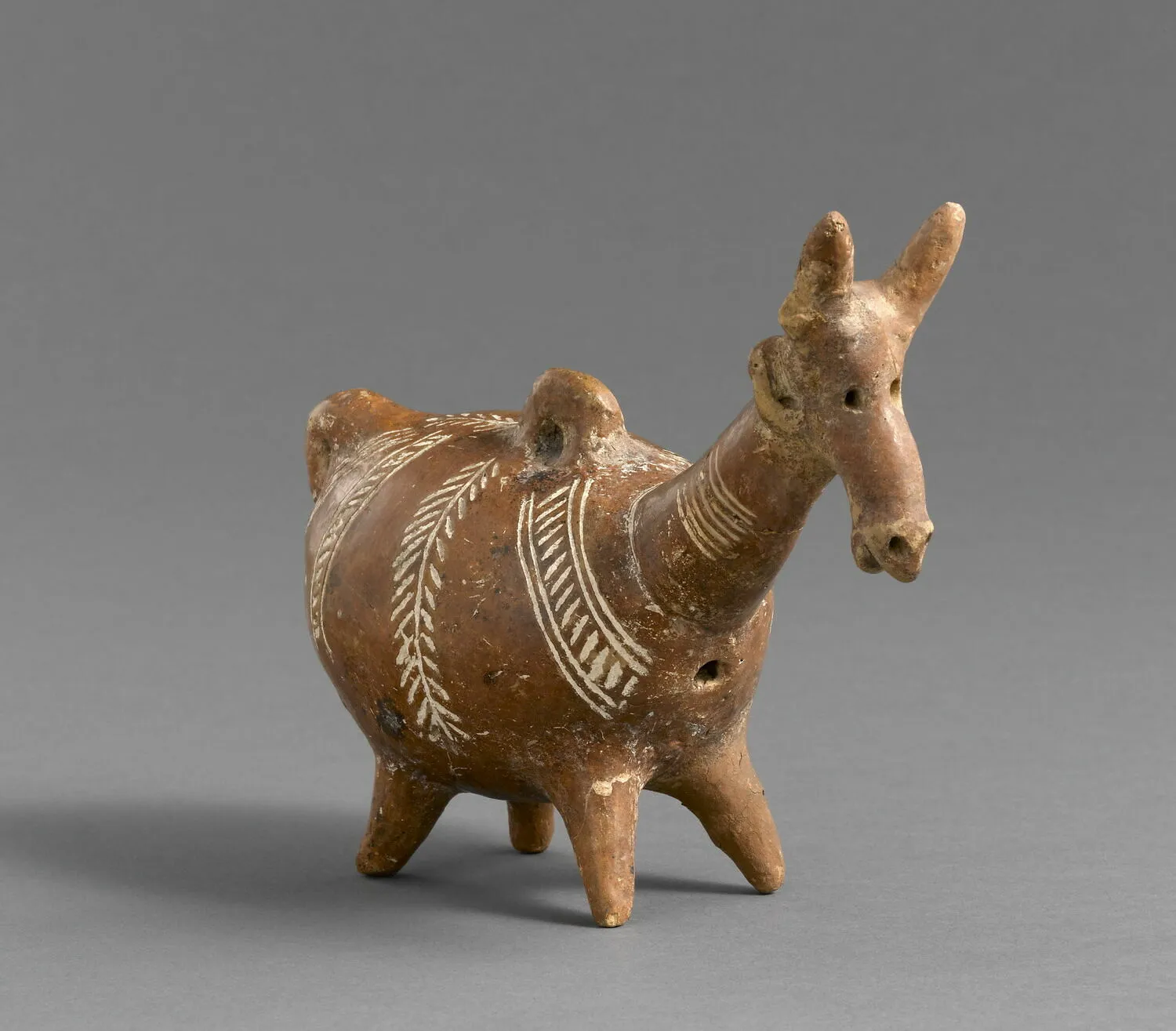 A Red Polished askos shaped as a long-headed deer with two ears, white-filled herringbone and concentric bands on its flank, standing on four legs. Louvre, AM 825, Middle Cypriot.
