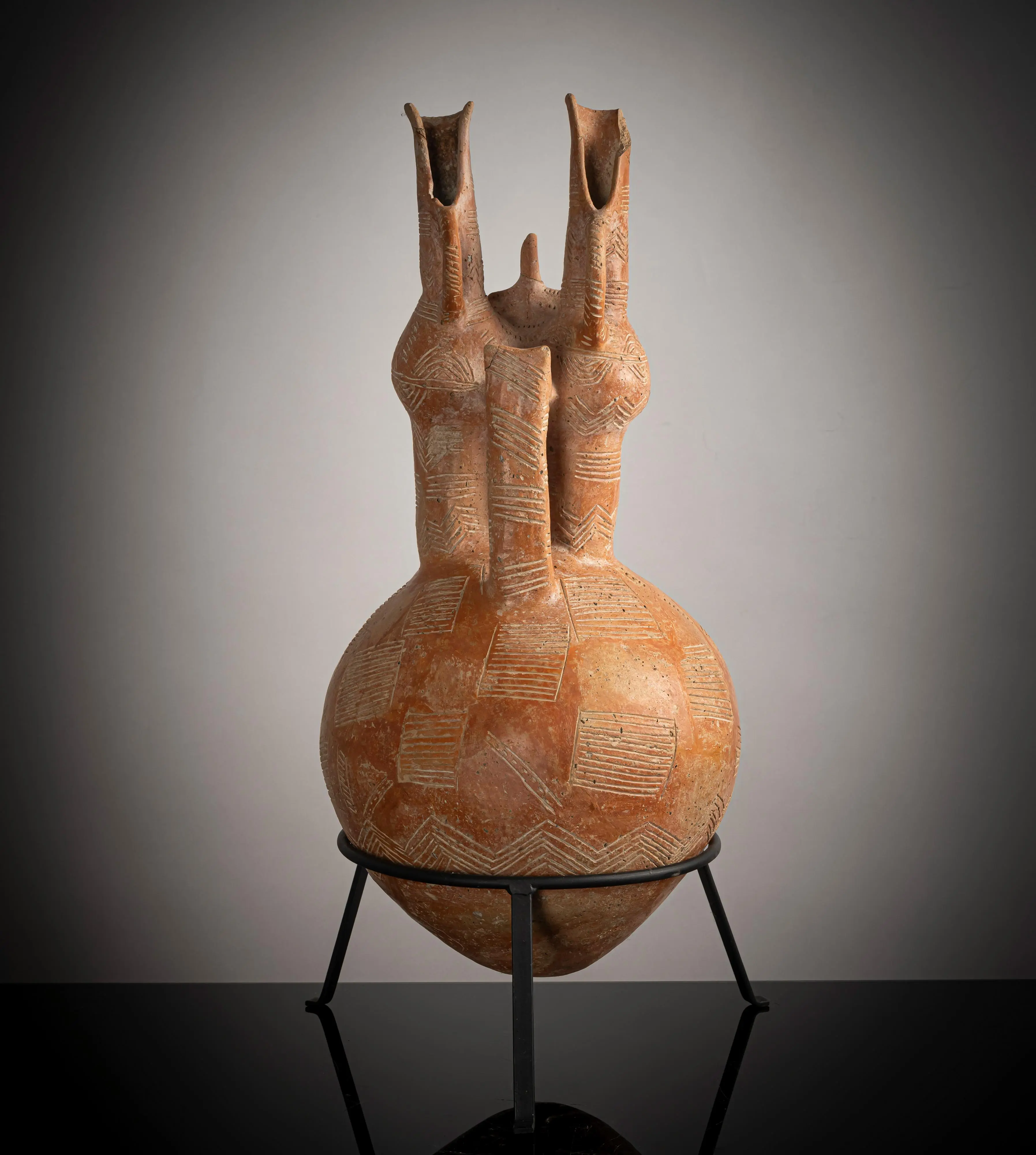 Back view of the jug showing the body covered in a patchwork of hatched squares and zigzag bands, white-filled incision against the even red slip, with the two cut-away necks above.