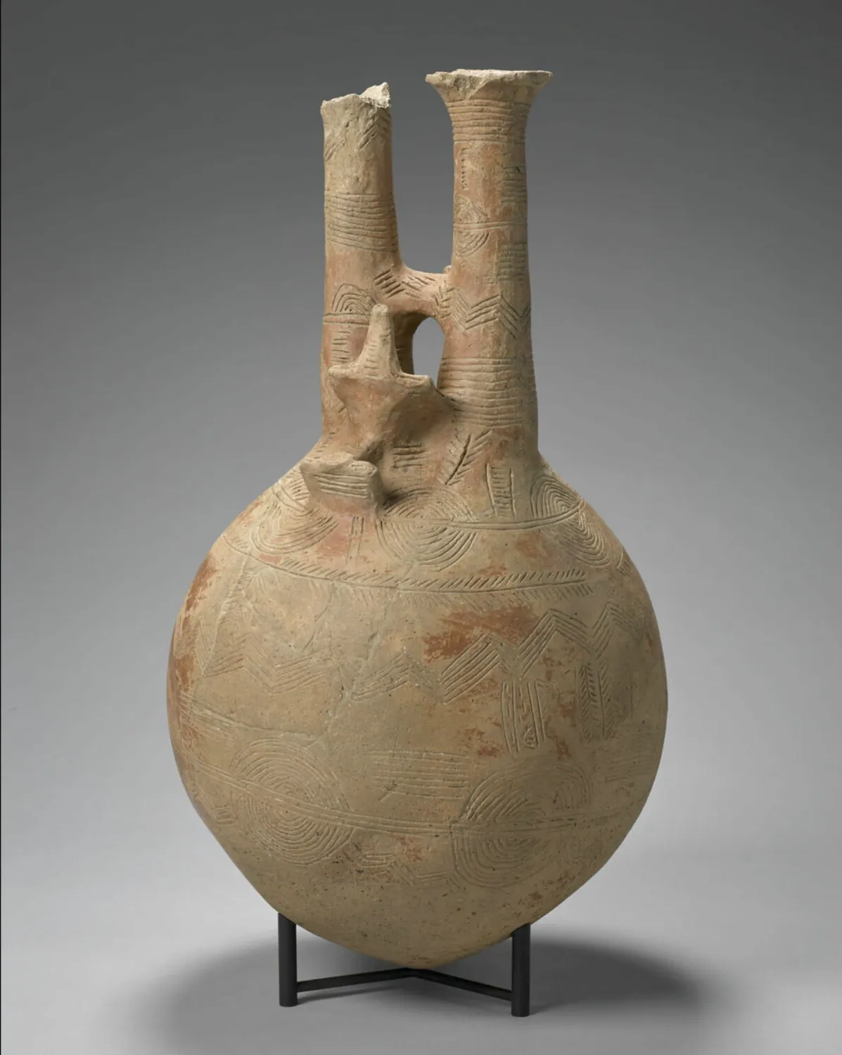 The Louvre's double-necked jug from Vounous Tomb 54 (inv. AO 17526), 50 centimetres tall: a single bird modelled at the front between the two necks, the buff body covered in fine incised pattern, on a black stand.