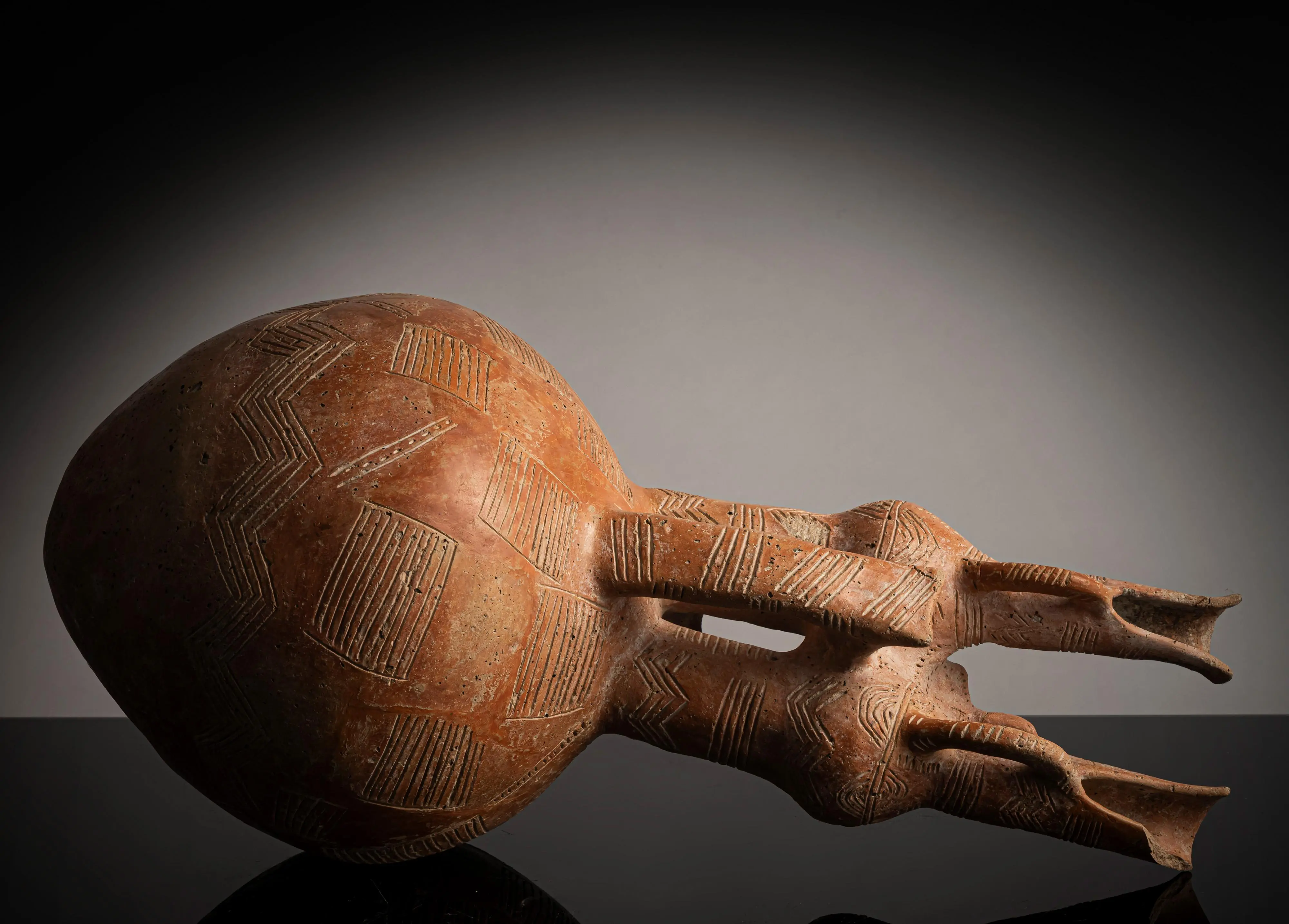 The jug photographed lying on its side, showing the two necks and the two forward-projecting birds in profile against the incised body.