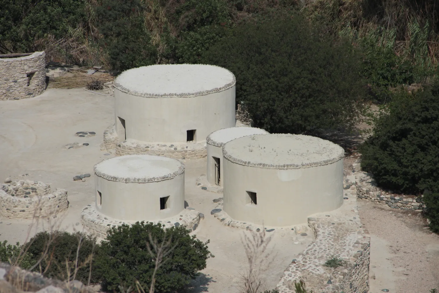 The replica houses at Khirokitia seen from above: round plastered buildings on stone bases with flat earth roofs edged by a rim of pebbles, built in the 1990s from the excavators' evidence after the old picture of domed huts was set aside.