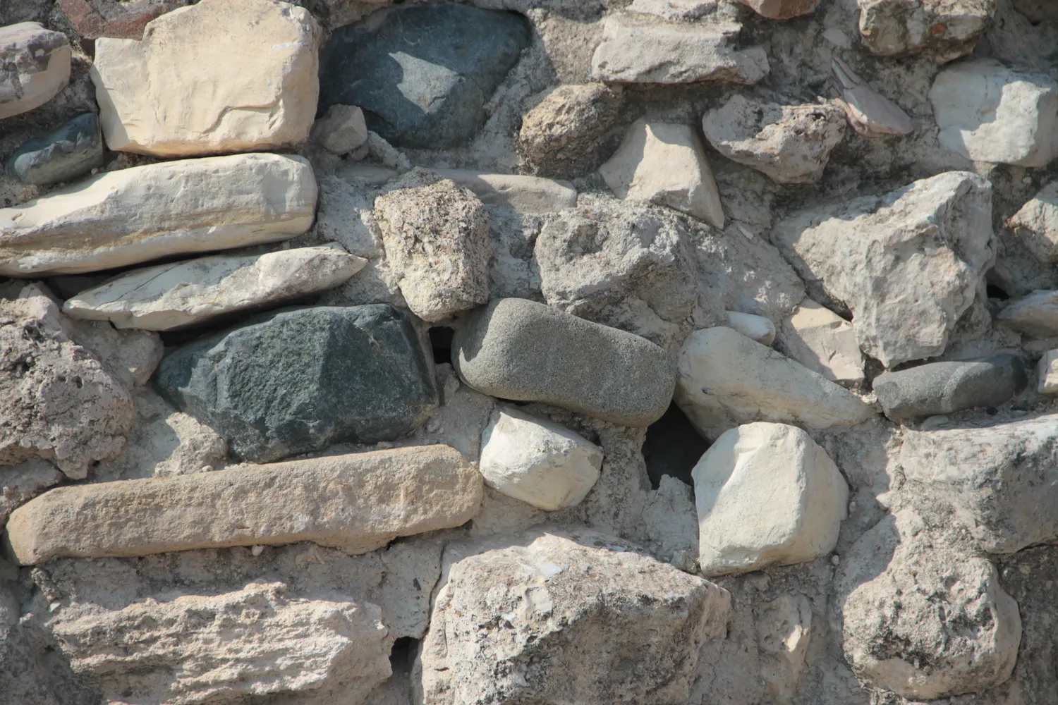 A wall at Khirokitia seen close up: rough pale limestone blocks gathered on the hillside and dark, rounded cobbles from the river below, laid in courses with earth packed between them. Photo: Anatoliy Smaga, CC BY-SA 4.0.