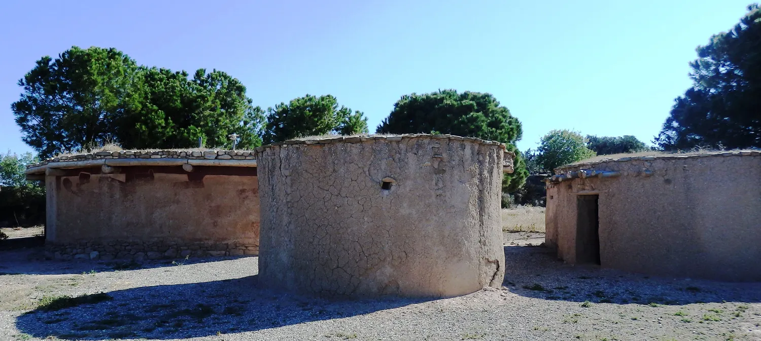 Three modern experimental round houses at the Lemba Experimental Village, built from 1988: on the left a mud wall on a stone socle under a flat roof with projecting eaves, in the middle a cracked mud wall with no stone footing, on the right a mud house with an open doorway. Photo: Hermann Junghans, CC BY-SA 3.0 DE.