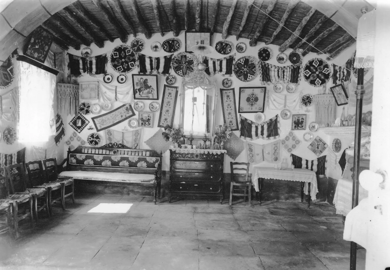 The best room of the village headman's house at Milia, photographed by the Swedish Cyprus Expedition between 1927 and 1931. The ceiling is the underside of the roof: timber poles laid close together, with reeds or split cane across them. The stone arch halves the span; the Bronze Age rooms of this lesson had none, and a pole's length set their width. Photo: John Lindros, Swedish Cyprus Expedition, CC0.