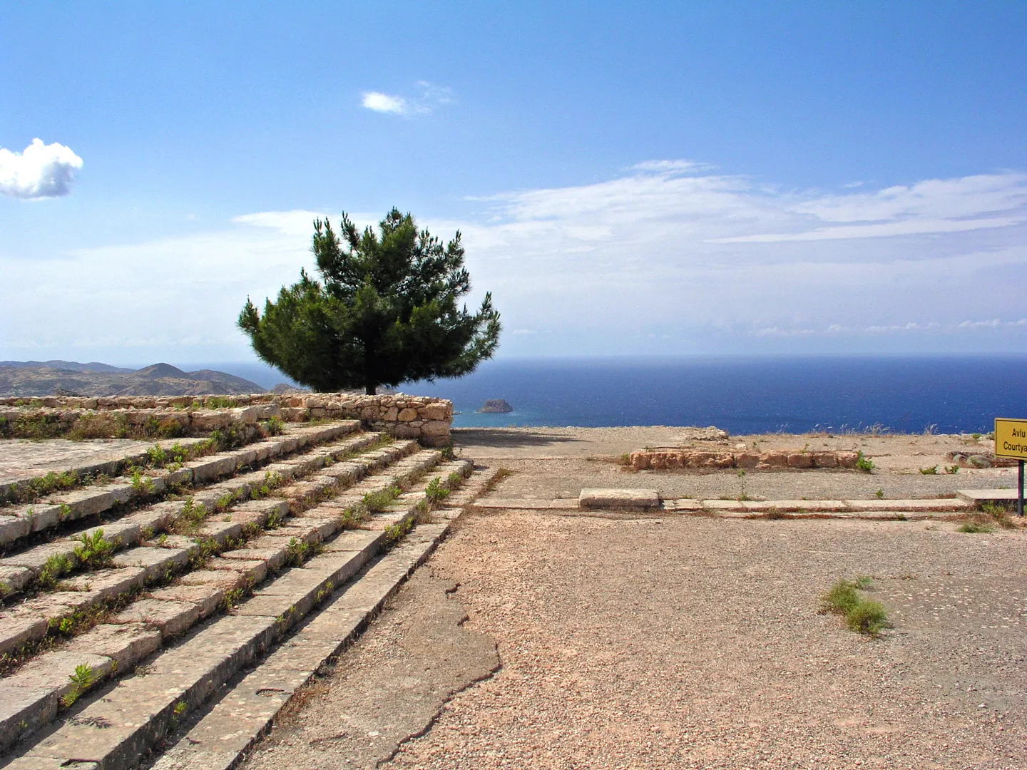 The broad stone staircase of the Vouni palace as it survives today, rising from the central court towards the hall suite, with a pine tree and the sea beyond. Photo: Cypern20, CC BY-SA 4.0.