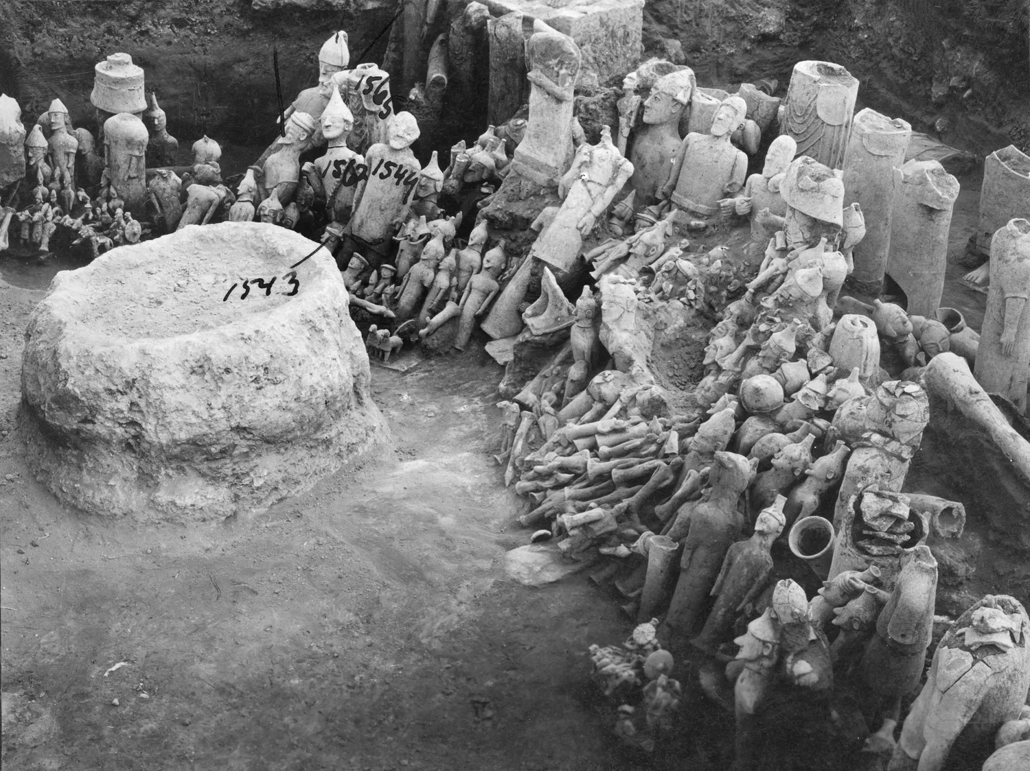 Ayia Irini during the Swedish excavation: the low stone altar in the foreground (numbered in ink) and, packed behind and beside it, terracotta figures of every size still standing or lying where they were found. Photo: John Lindros, Swedish Cyprus Expedition, CC0.