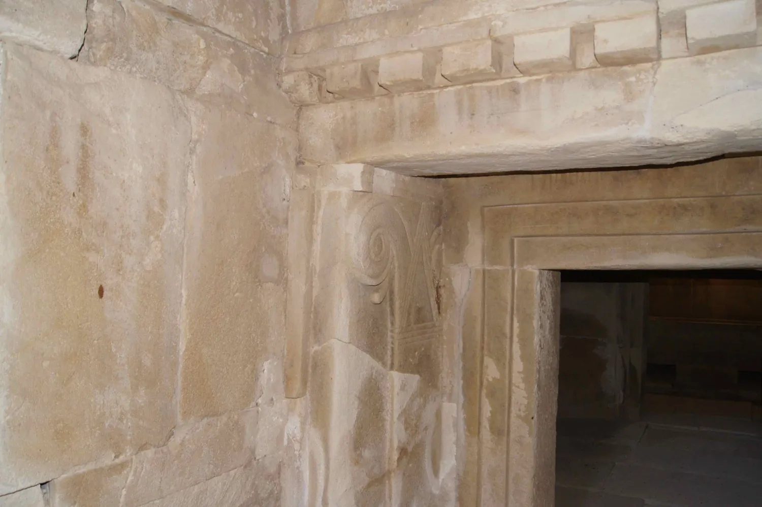 An inner doorway in one of the royal tombs at Tamassos, as restored: a recessed frame of stepped mouldings, a row of carved beam-ends above the lintel, and at the left a flat pilaster topped by a volute capital, all in dressed limestone. Photo: Rjdeadly, CC BY-SA 4.0.