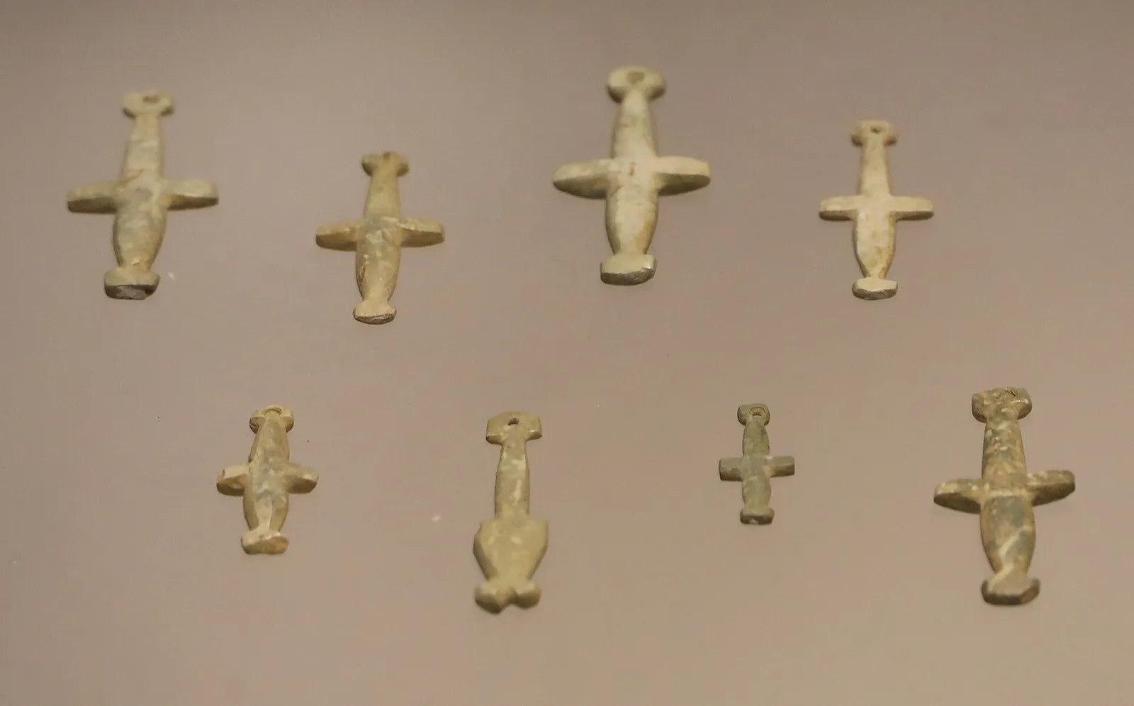 Eight small pale green picrolite cross-shaped pendants of different sizes arranged on a beige board