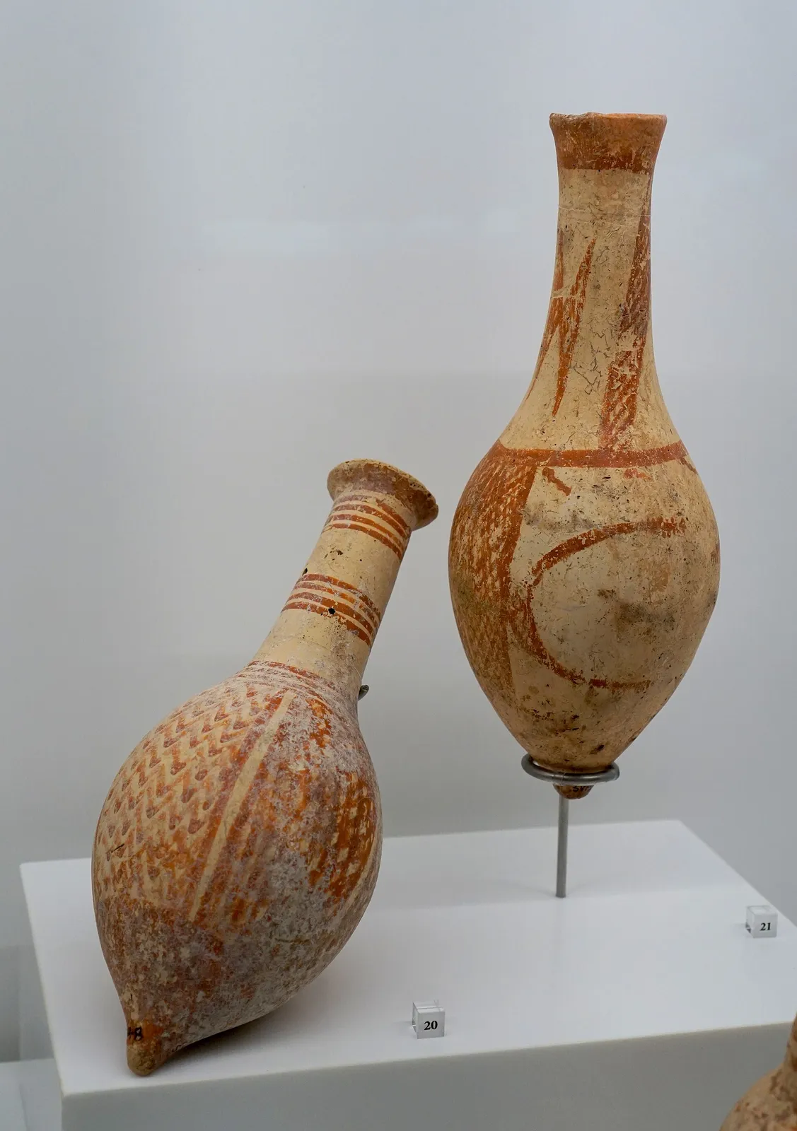 Two long-necked flasks, one with a pointed base, painted in orange-red on a pale ground with lattice bands and a crescent