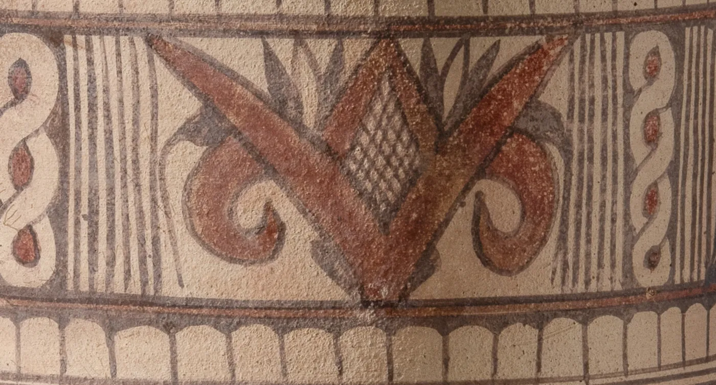 Detail of the neck above one handle: a red volute flower with a latticed lozenge at its heart, between columns of S-spirals and ruled lines.