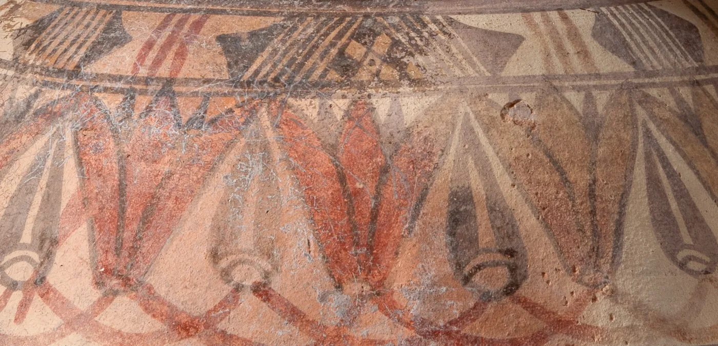 Detail of the shoulder frieze on face A: an open lotus washed in red, with a dark bud beside it, each rising from a small ring.