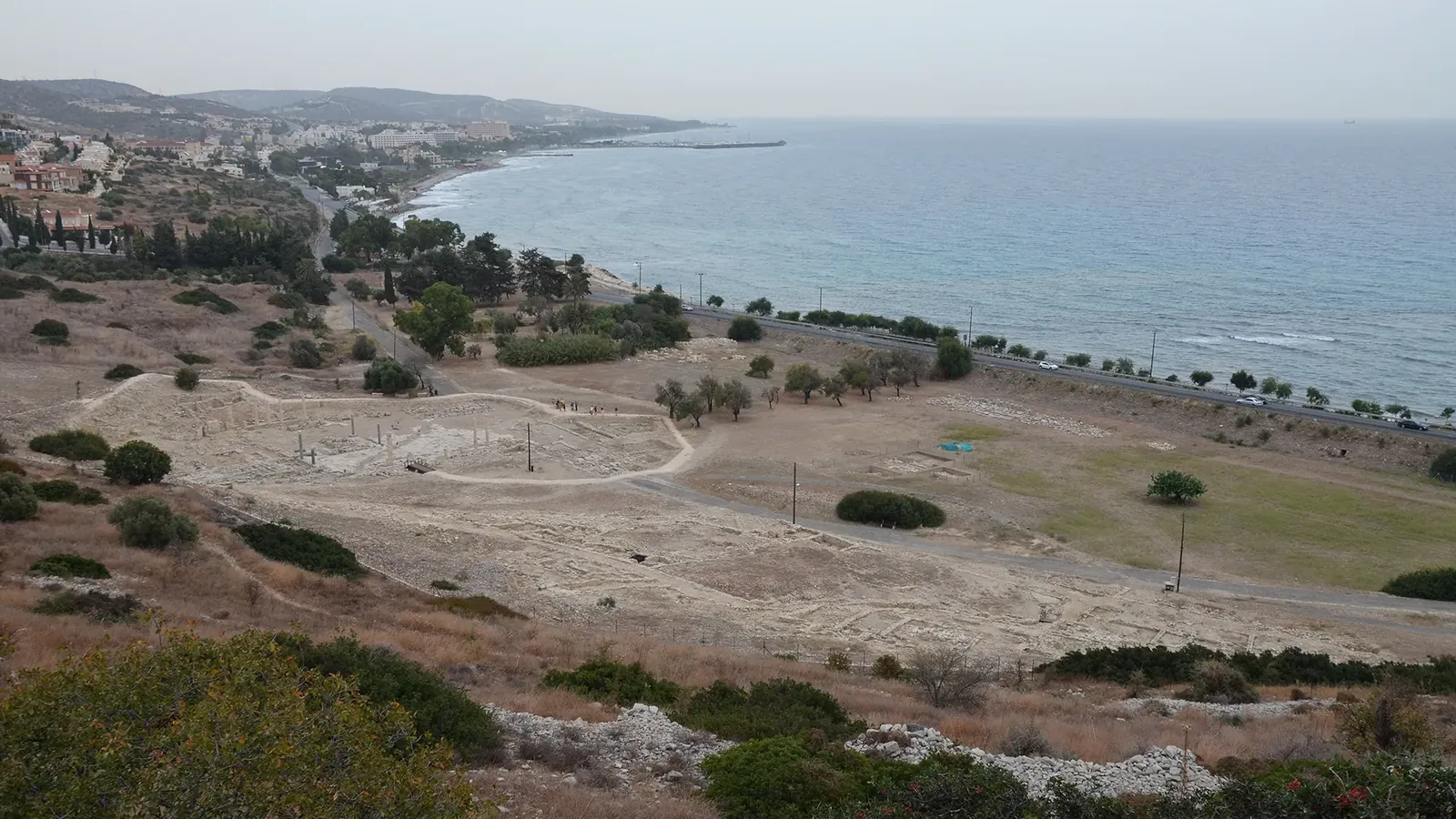 Excavated stone foundations and standing columns of the lower city at Amathus, seen from the hill above, with the coast road and the sea beyond