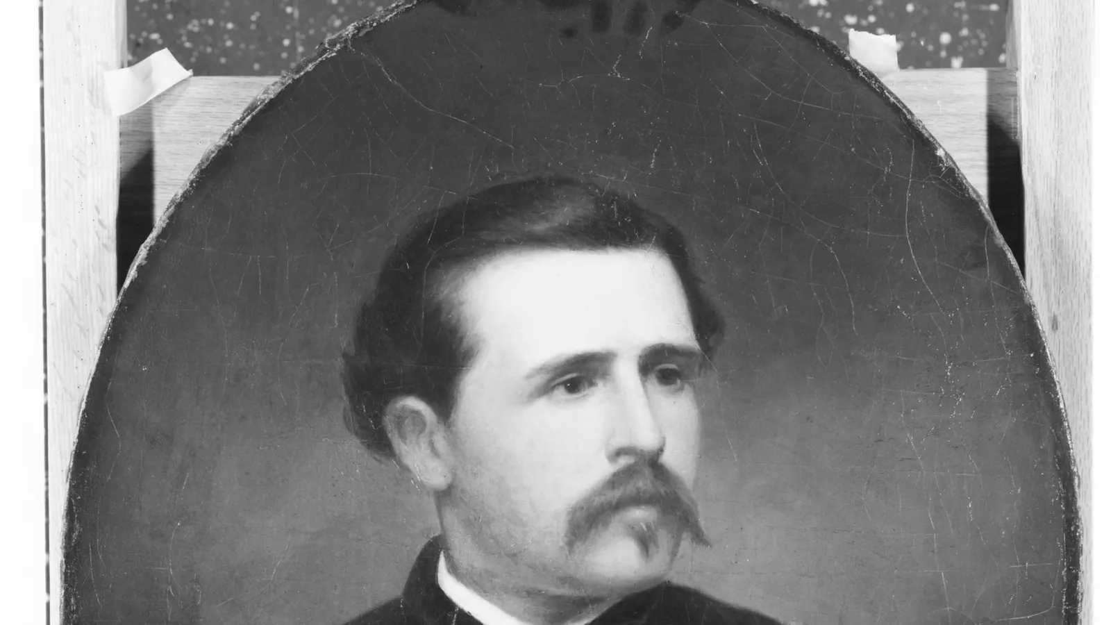 Black-and-white photograph of an oval painted portrait of Luigi Palma di Cesnola as a young man with a moustache and dark jacket, propped against a wooden frame