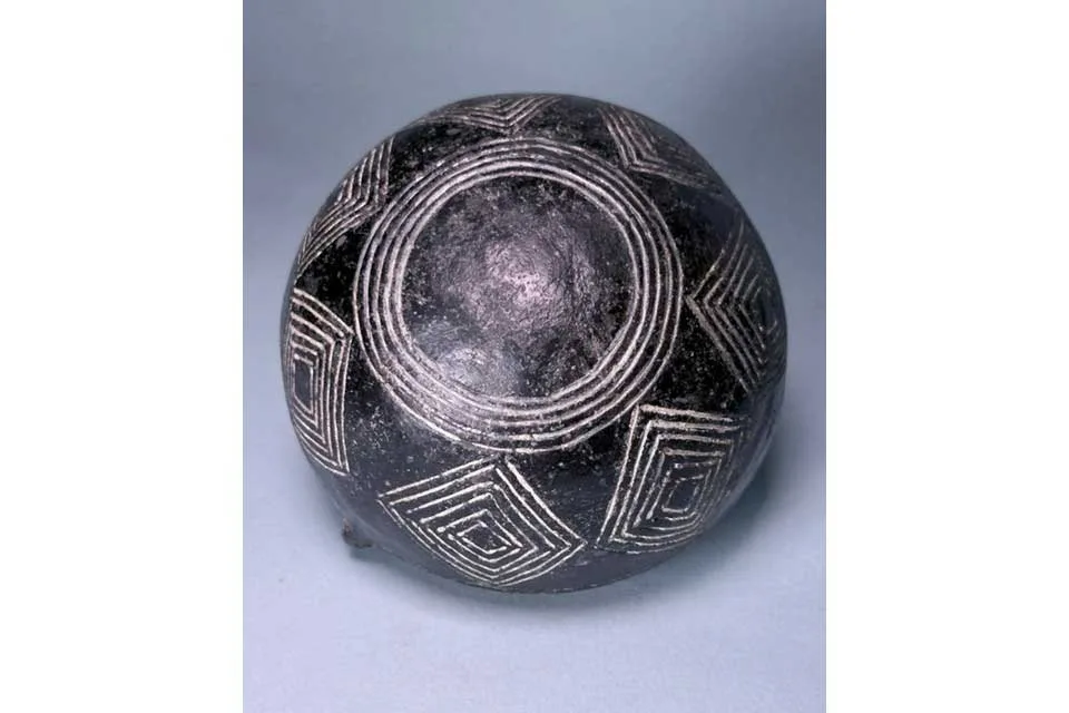 Black bowl seen from below, its surface incised with white-filled concentric circles and chevrons