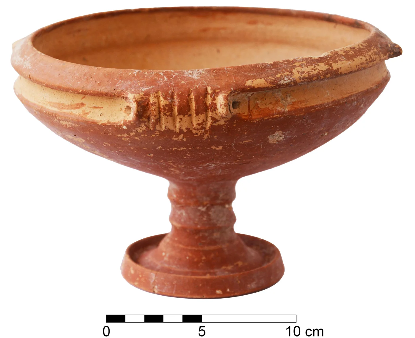 A red-slipped pottery bowl on a tall ringed stem and flat foot, with a moulded band below the rim and a small ridged lug, photographed on white with a 10 cm scale