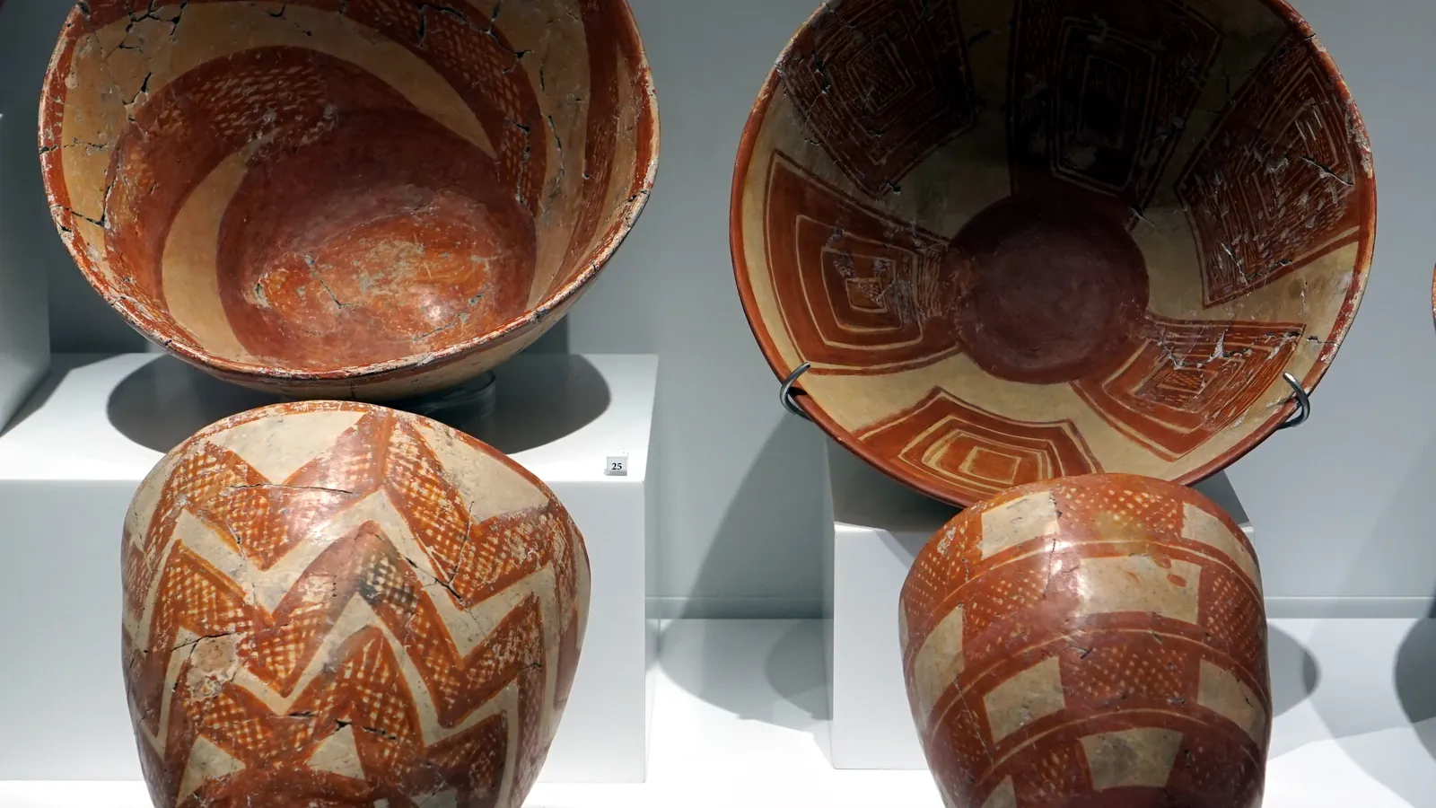 Four Chalcolithic bowls from Kissonerga painted in red with zigzag, lattice and nested-square patterns on a pale ground, on white museum plinths