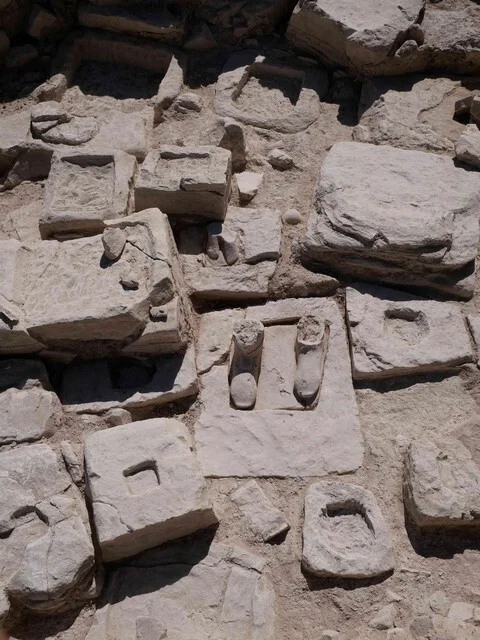 Rectangular limestone blocks packed closely in the earth, seen from above; the block in the centre still carries the two feet of a lost statue