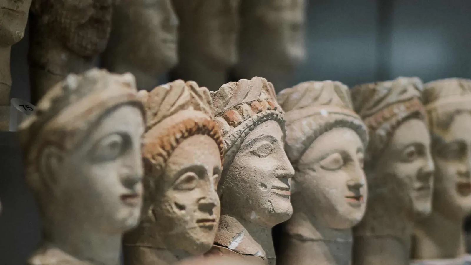 Rows of small ancient Cypriot stone heads on display, several wearing wreaths with traces of red paint, the nearest in sharp focus