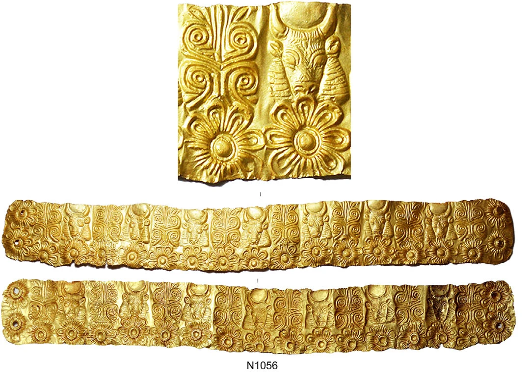 Close-up of embossed gold sheet showing a bull's head seen from the front with a disc between its horns, a palm-like plant and two eight-petalled rosettes, above both faces of a long gold band repeating the same design