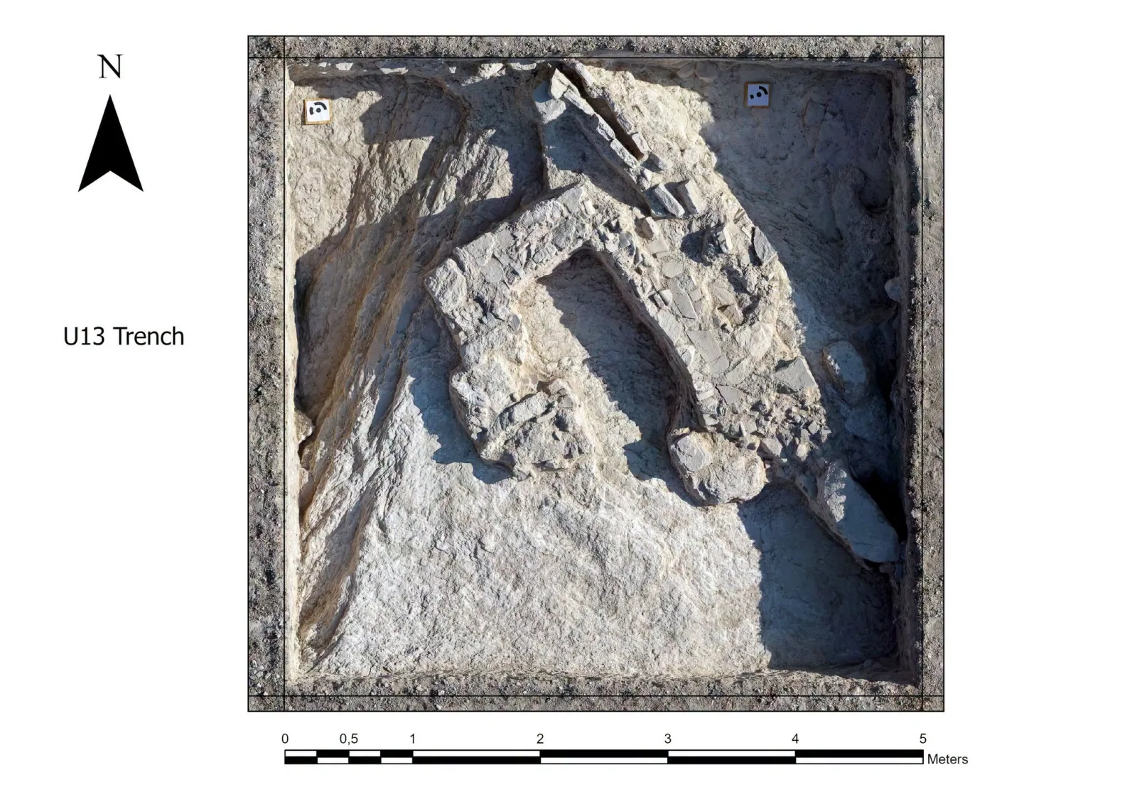 Overhead view of a square trench cut into pale bedrock, with a U-shaped wall of rough stones and a row of stone slabs leading to it from the north edge, a north arrow and a 5-metre scale bar