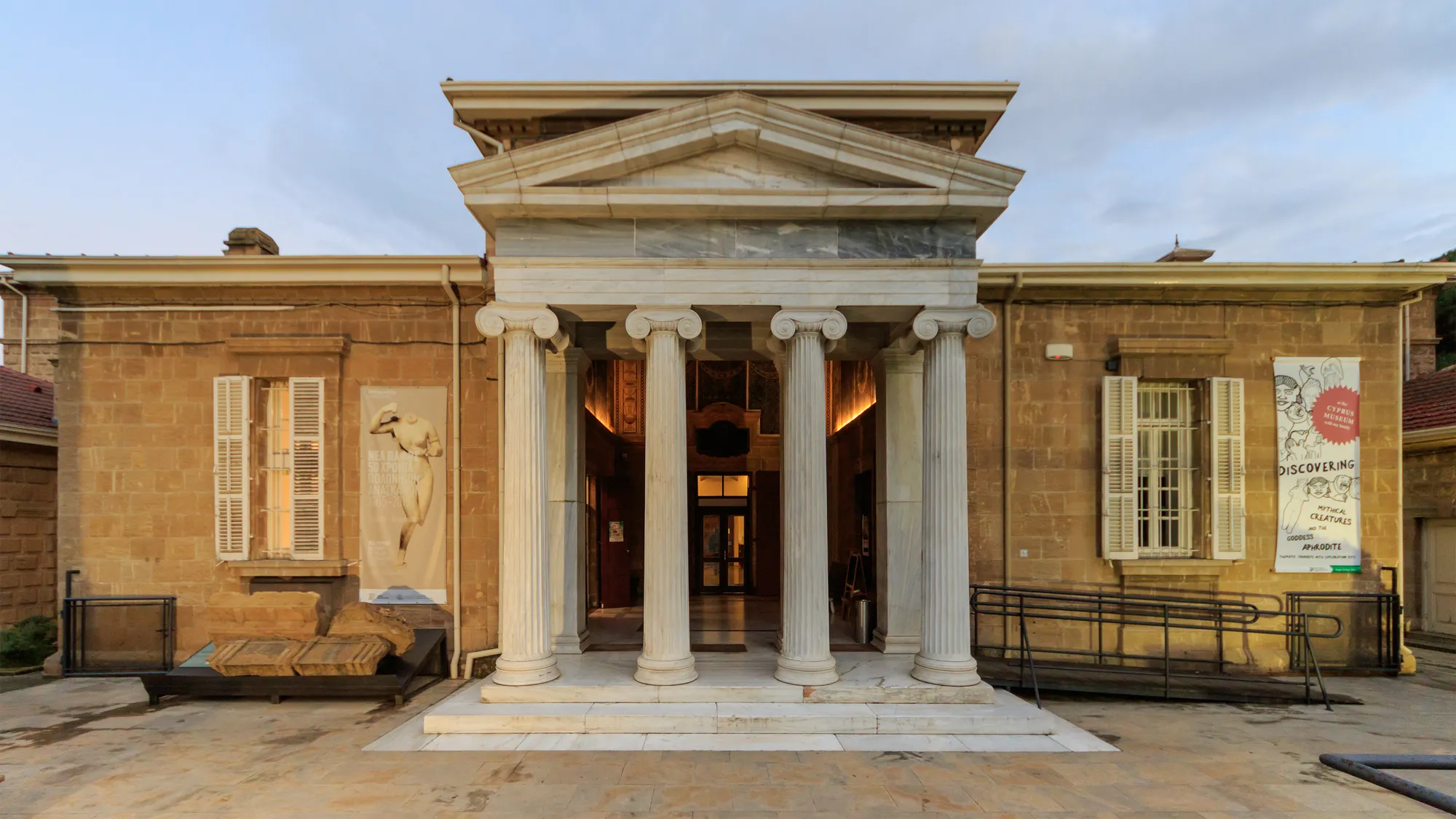 Classical-style portico with Ionic columns at the entrance of a single-storey stone museum building, with palm trees in front