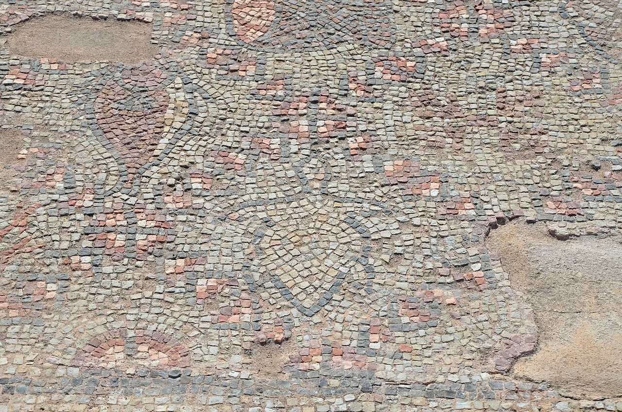 Close view of a worn floor mosaic of small grey, white and pink stone cubes forming a geometric pattern with leaf shapes