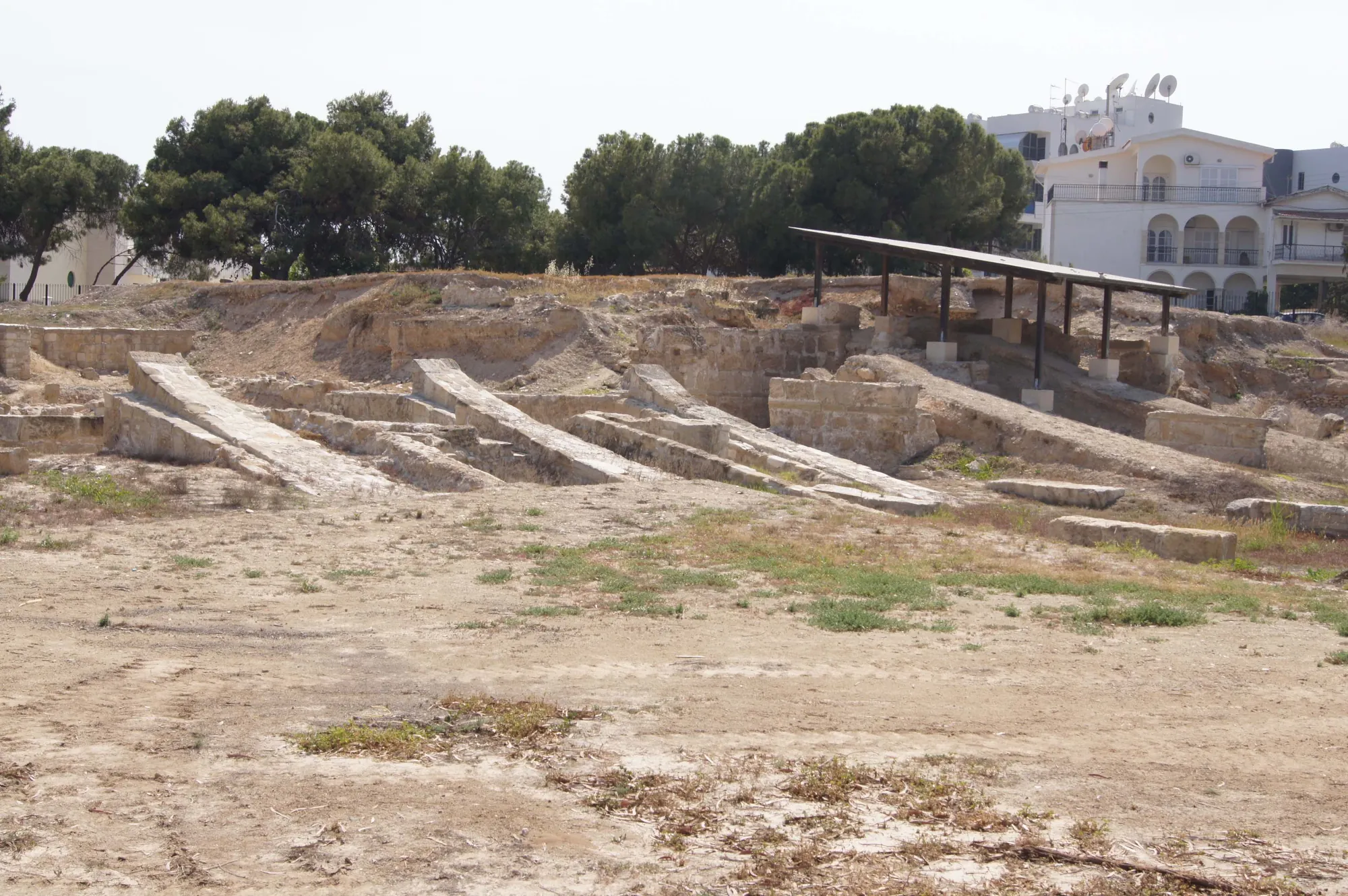 Several parallel sloping stone ramps in an excavated pit, a lightweight roof and white building behind