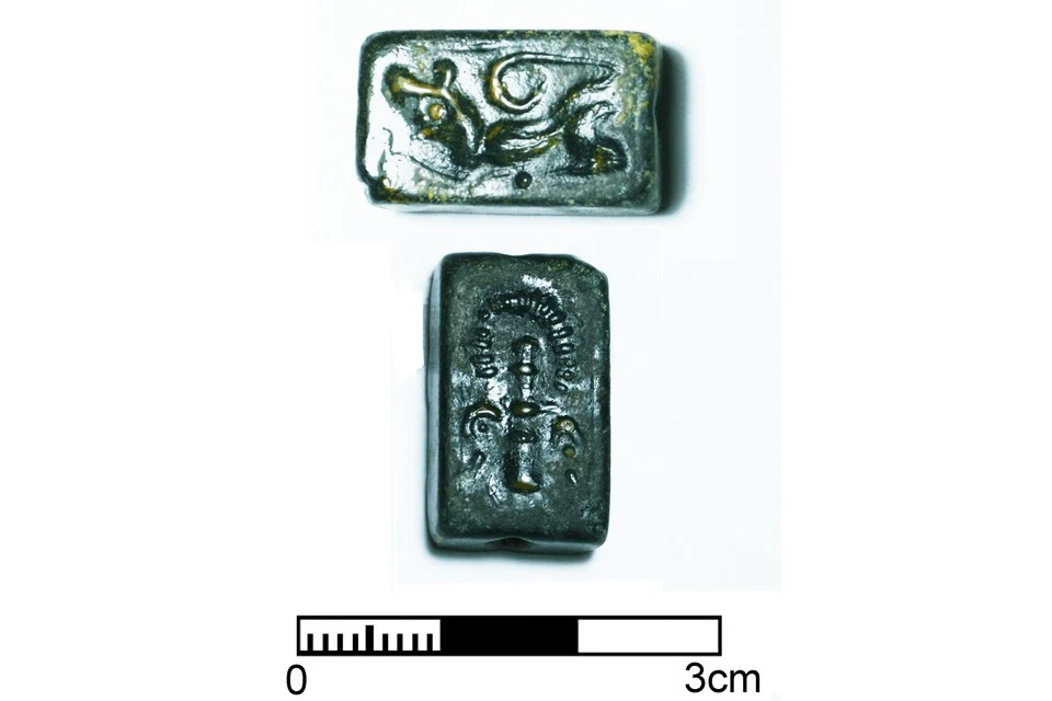 Two faces of a small dark rectangular stamp seal, one cut with a crouching animal and the other with an upright figure, above a 3 cm scale bar