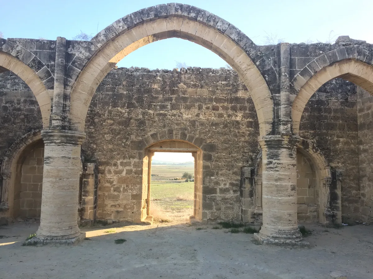 Pointed stone arches of a roofless Gothic church framing a view over a flat, dry plain with low hills behind